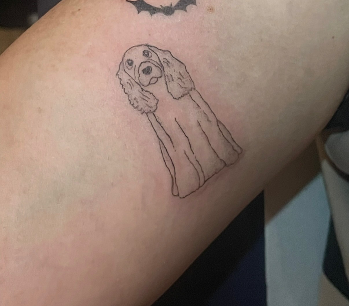 Fine line tattoo of a spaniel dressed as a ghost with a tiny bat