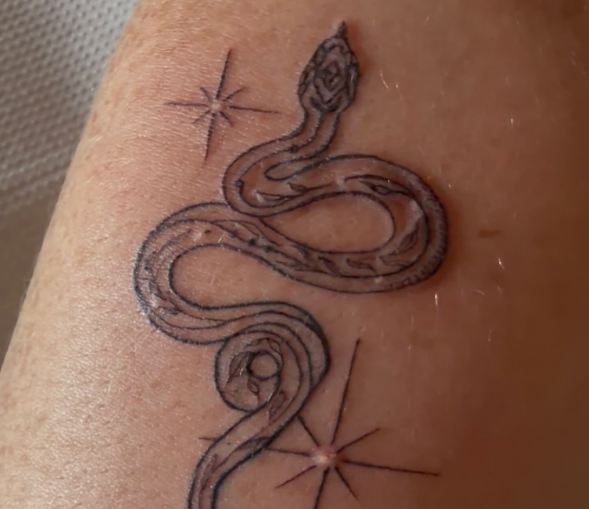 Fine line snake tattoo with sparkle stars on a forearm